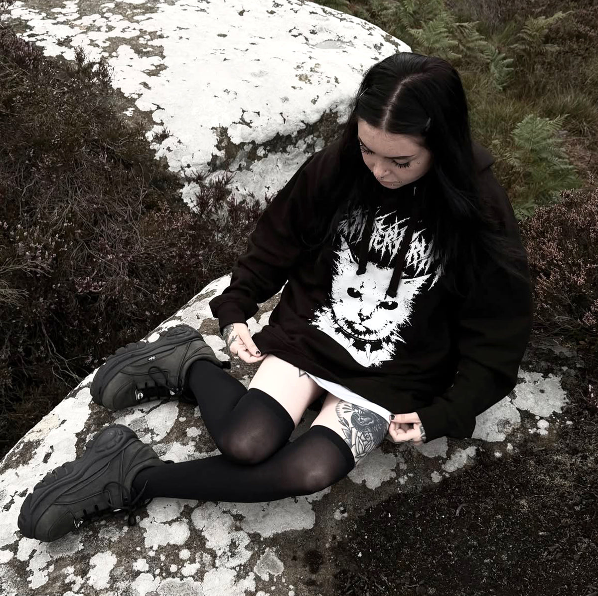 Model sitting outdoors wearing a black MEOW Hoodie with a white cat graphic