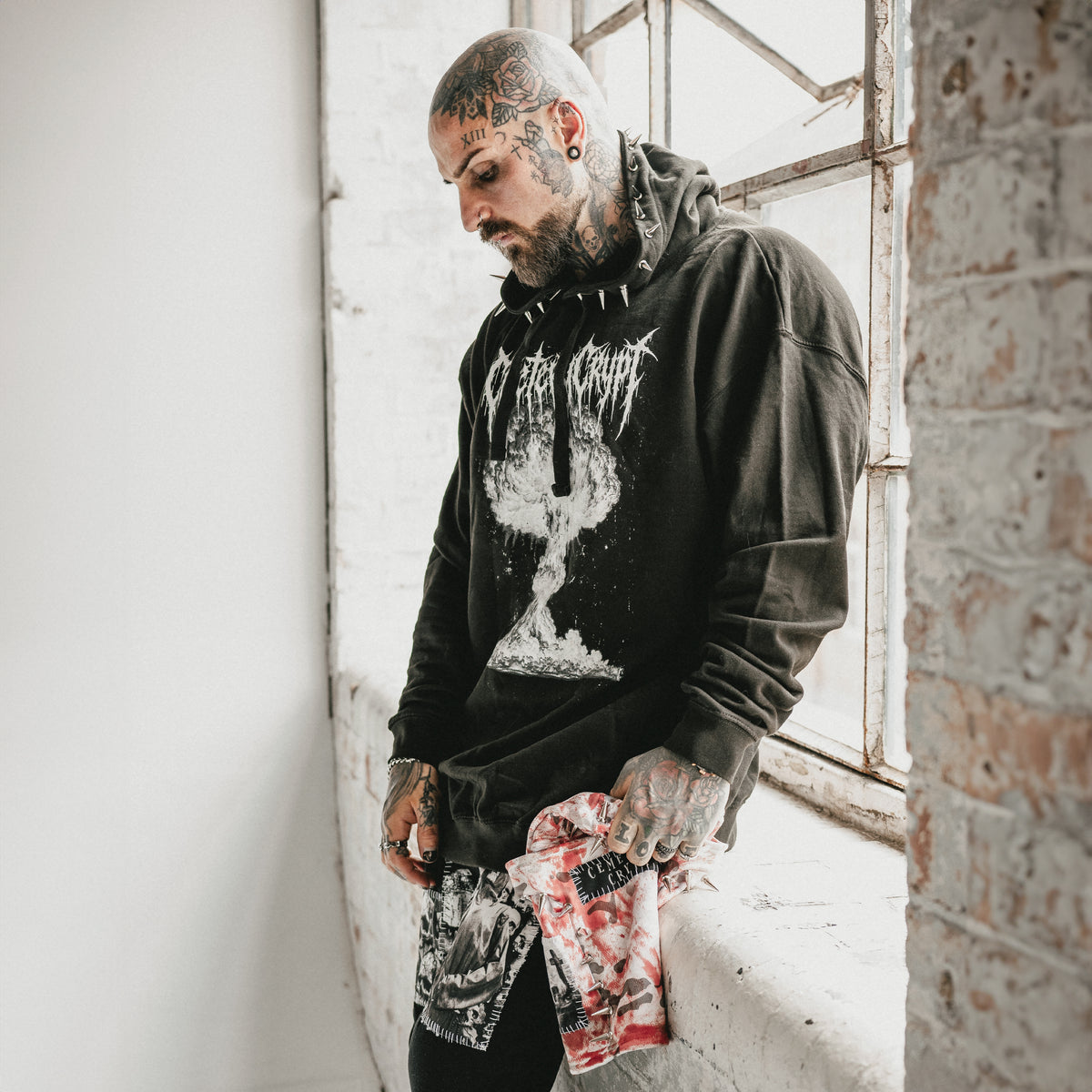 Tattooed model wearing the black M.A.D Hoodie by an industrial window