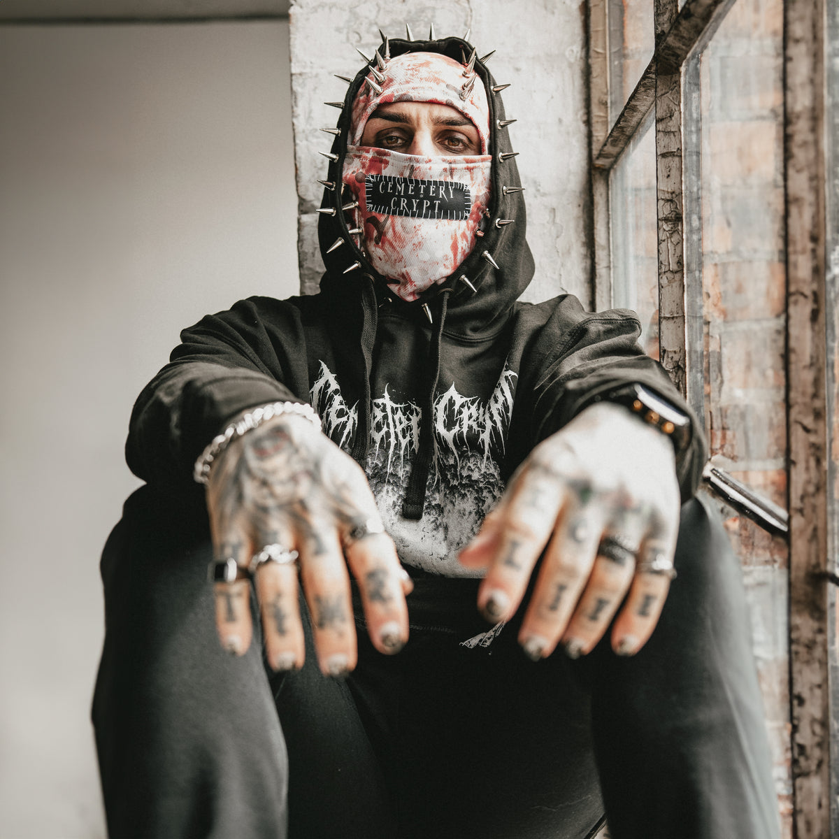 Seated model wearing the Bloody Snow Spiked Balaclava with a black graphic hoodie