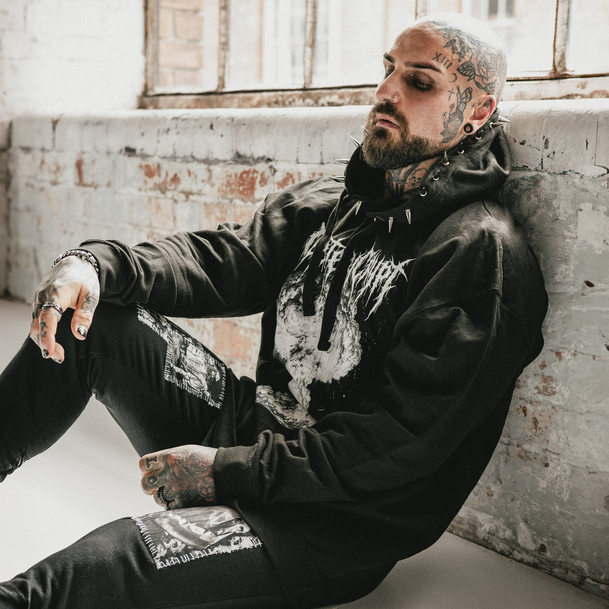 Tattooed model seated in the black M.A.D Hoodie with spiked hood