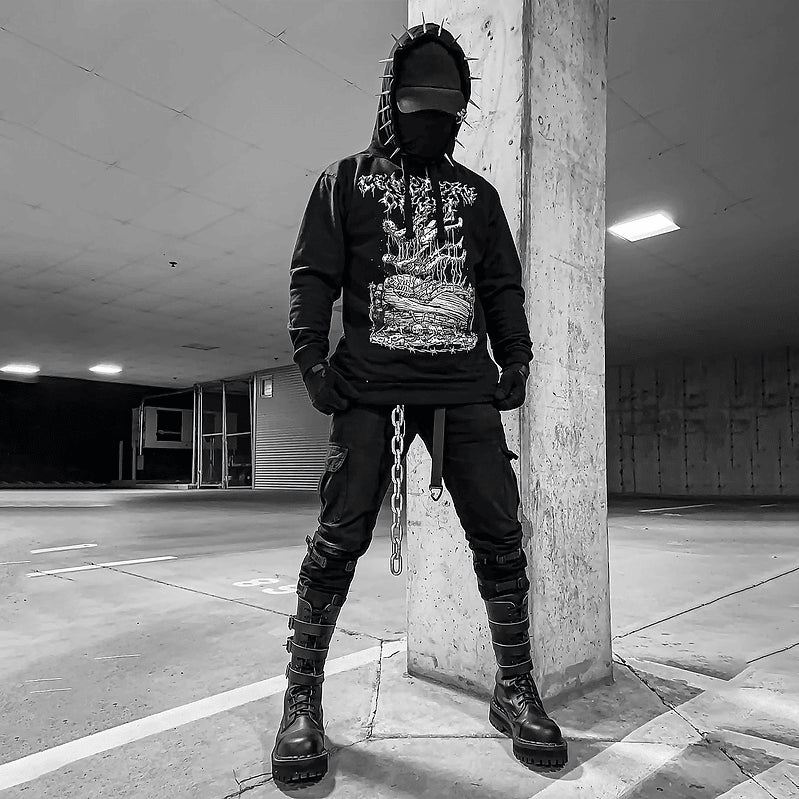 Full view of a masked model wearing the Decay Hoodie in a car park, showing its white graveyard print