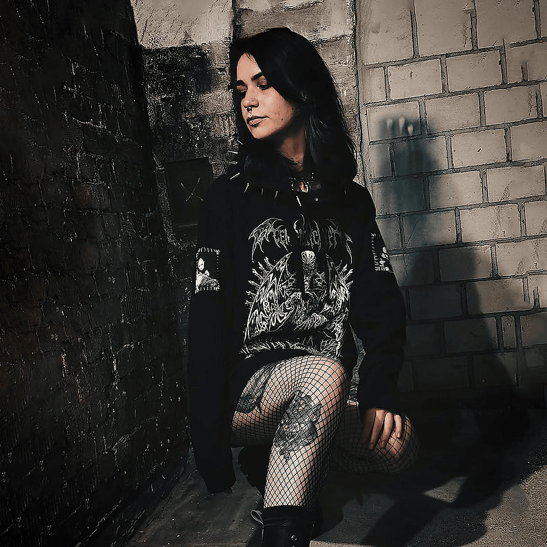 Model kneeling beside a brick wall wearing the Dracula Hoodie with its white and green front print visible