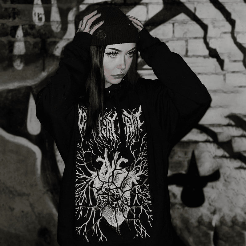 Model adjusting their hat while wearing the Fractured Heart Hoodie, showing the white heart print