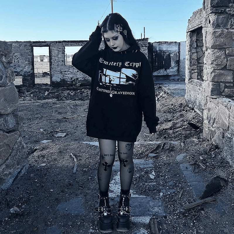 Model wearing the black Gravedigger Hoodie outdoors, showing its white grave graphic and chest lettering