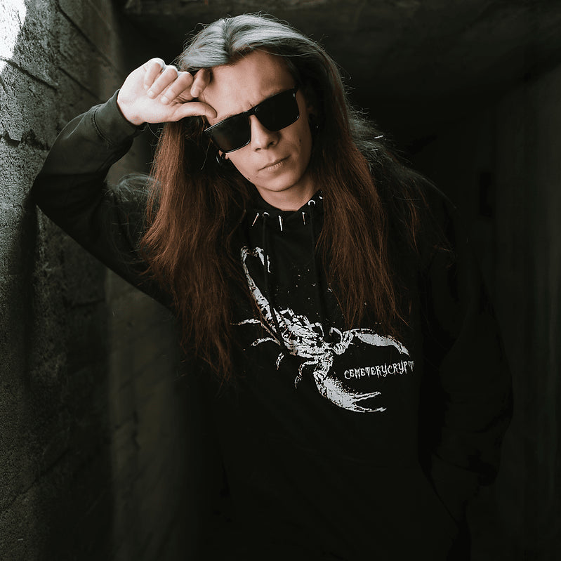 Close view of a model wearing the Scorpion Hoodie with a hand raised above their sunglasses