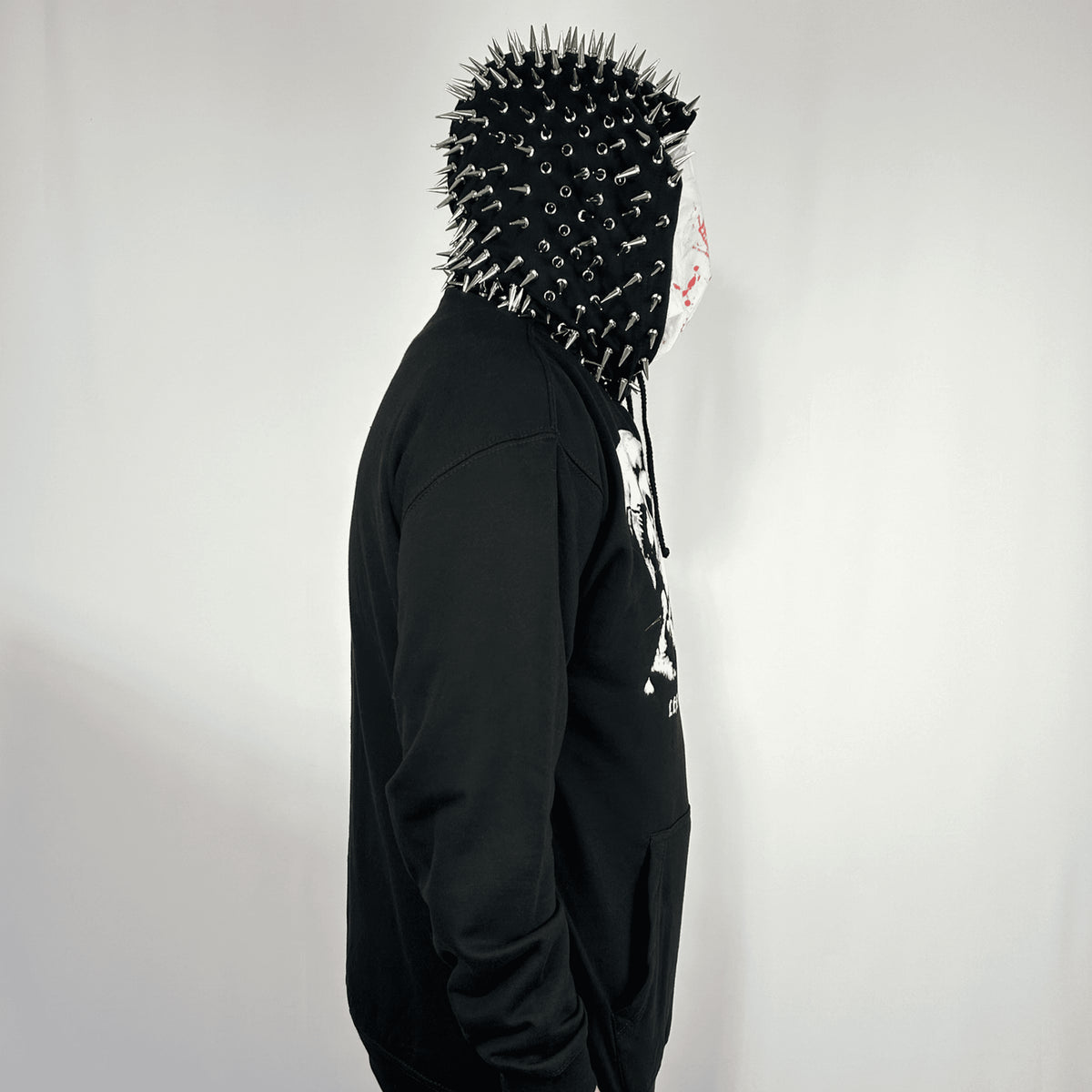 Side view of a model wearing the Terror Hoodie with the spiked hood raised and hands in the front pocket