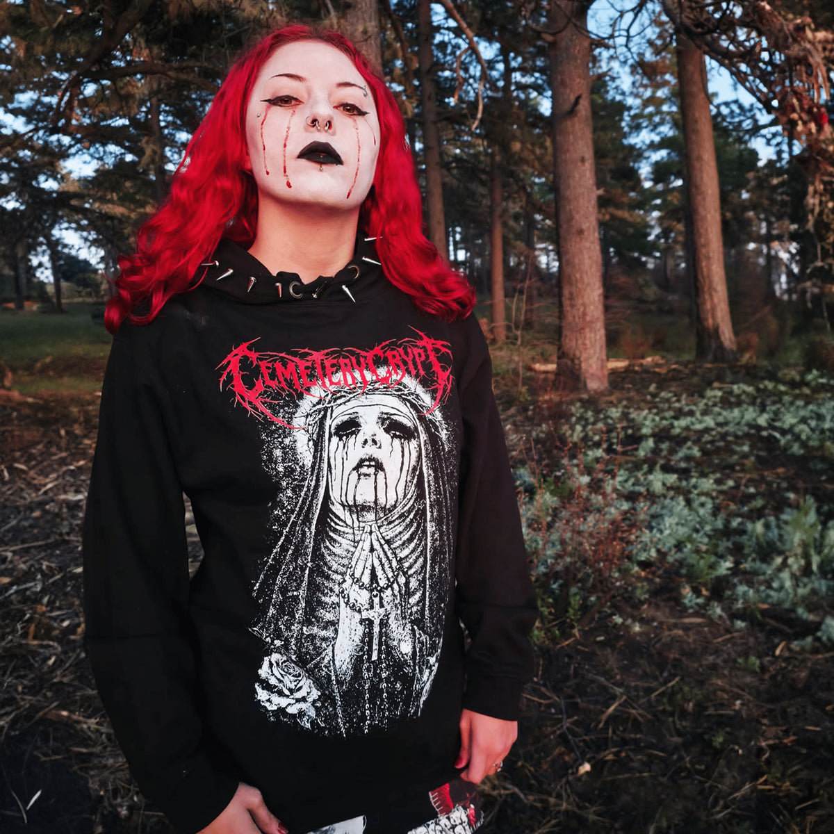 Model wearing the black Unholy Devotion Hoodie with a veiled-figure print and red lettering outdoors